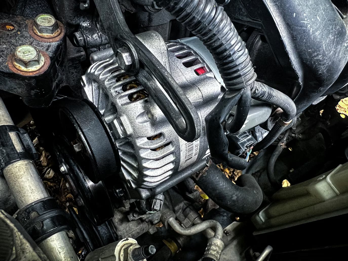Acercamiento a un alternador automotriz con su banda serpentina y polea, el componente del sistema de carga que se diagnostica junto con la batería