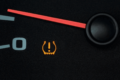 Amber TPMS tire pressure warning light symbol illuminated on a vehicle dashboard gauge cluster